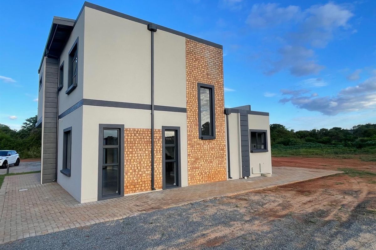 A modern double-storey residential exterior featuring a combination of face brick and plastered finishes with contemporary aluminium window frames and paved surrounds.