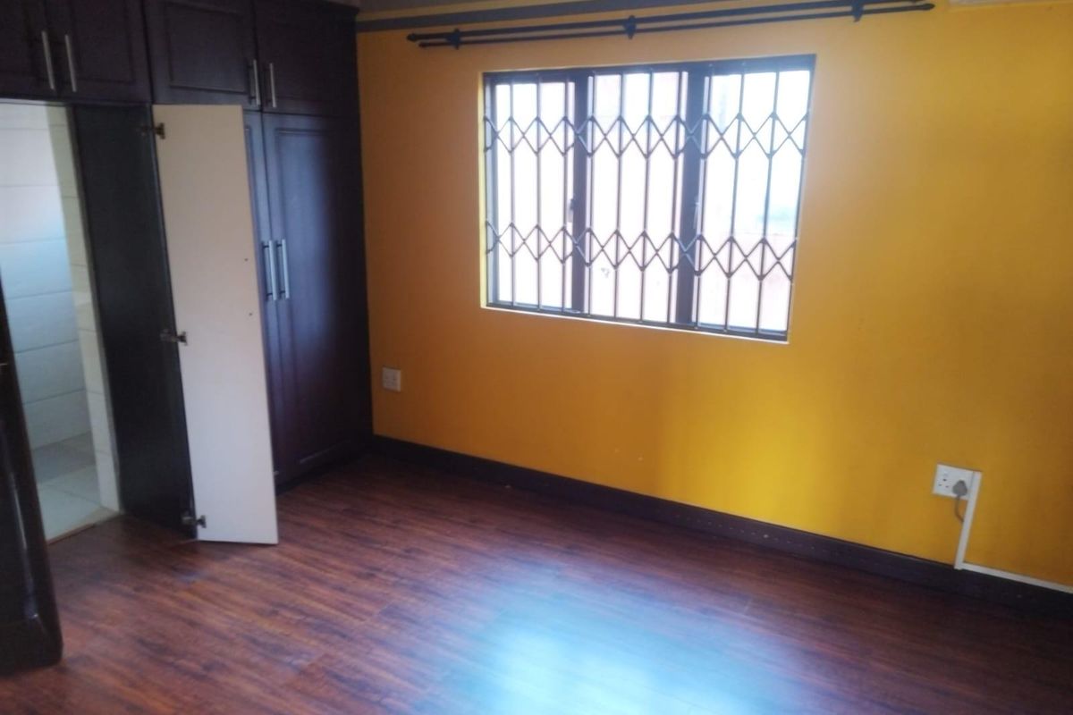 A bedroom featuring dark wood-look laminate flooring, built-in dark cabinetry, and a window fitted with security bars.