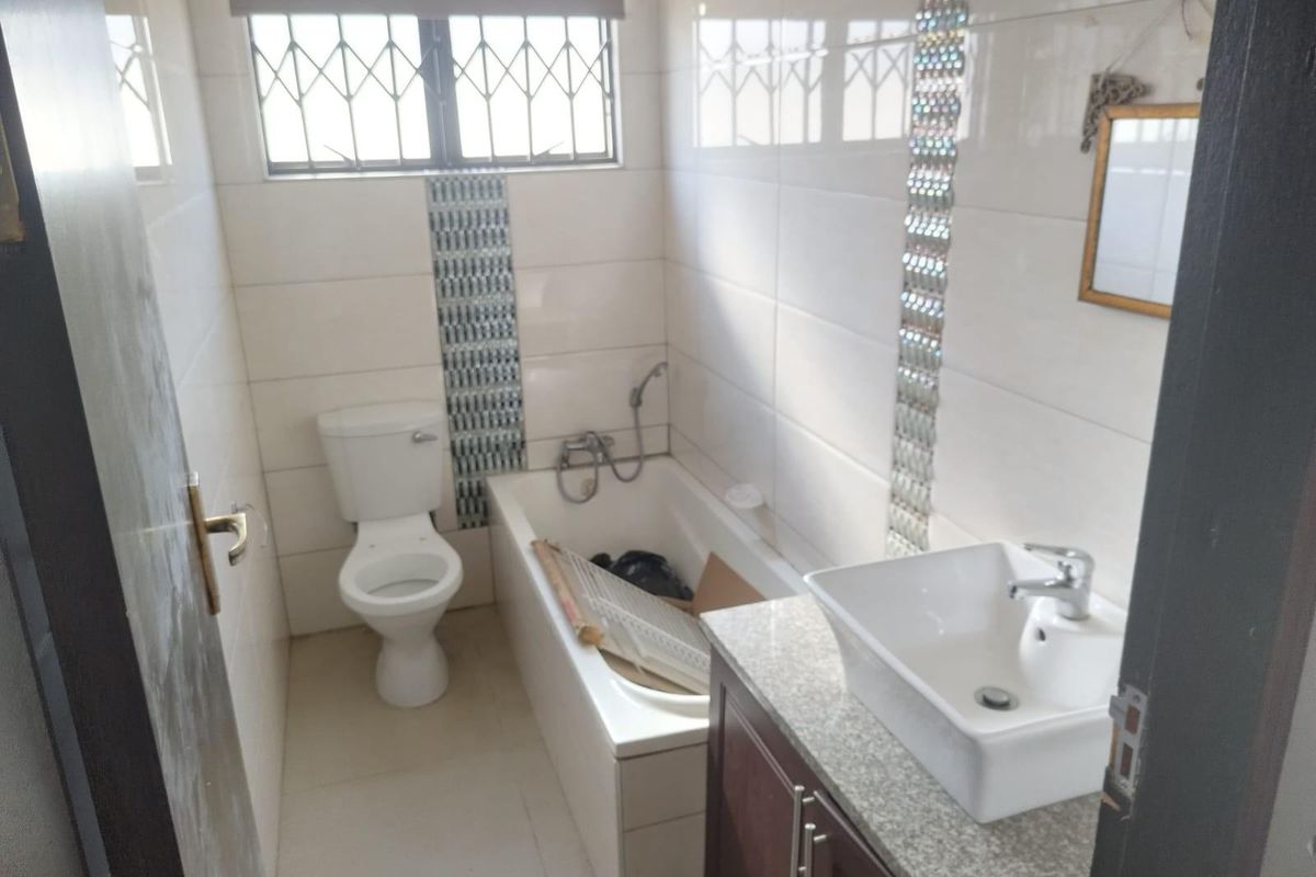 A compact bathroom featuring a built-in bathtub, a modern vessel sink on a vanity cabinet, and a standard toilet with tiled walls.