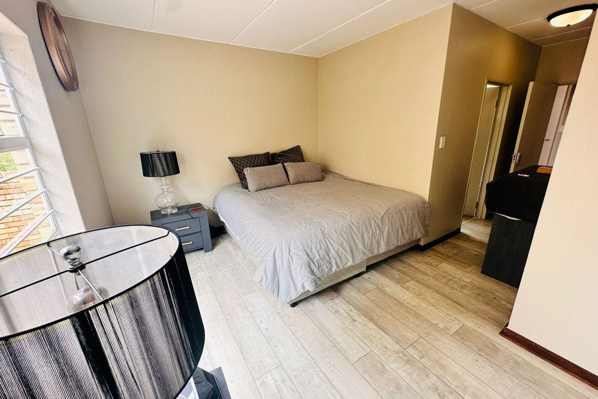 A bedroom featuring light wood-look flooring, neutral wall tones, and a window with security bars, providing a functional and simple living space.