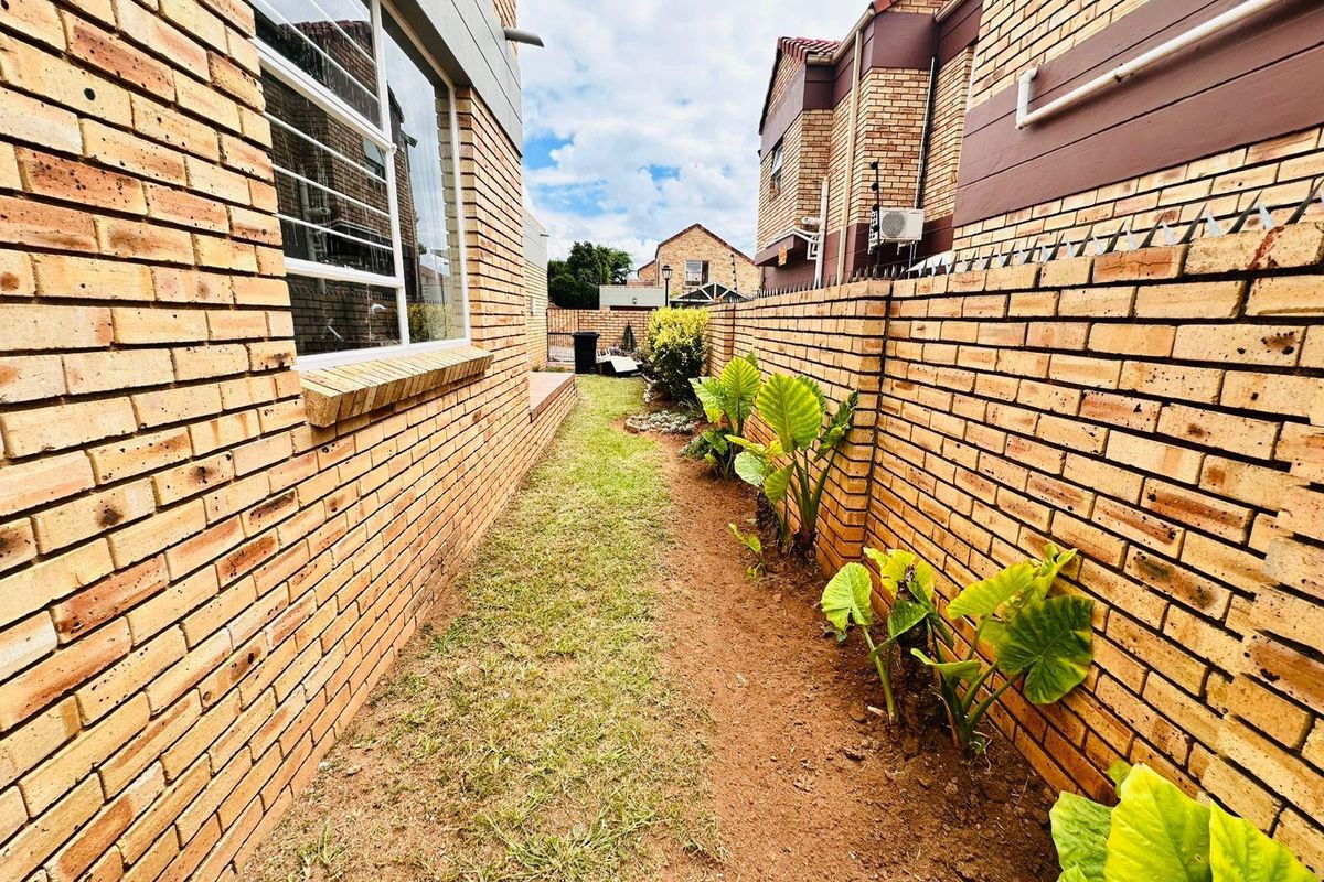A narrow side garden passage featuring face brick walls, a grass strip, and established perimeter planting.