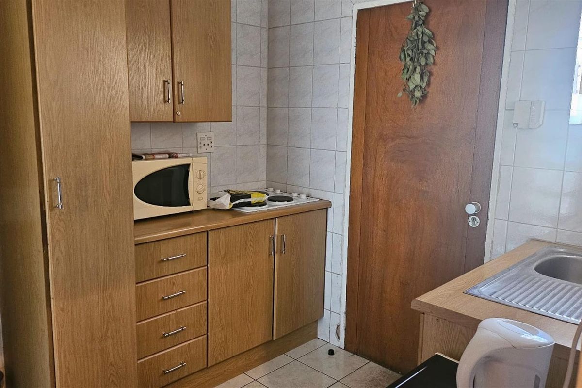 A compact kitchen featuring laminate cabinetry, a built-in hob, tiled backsplash, and a stainless steel sink with tiled flooring.