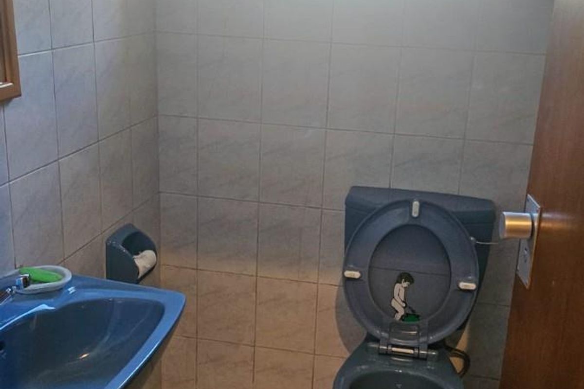 A compact bathroom featuring dated blue sanitaryware, tiled walls and floors, and a window with security bars.