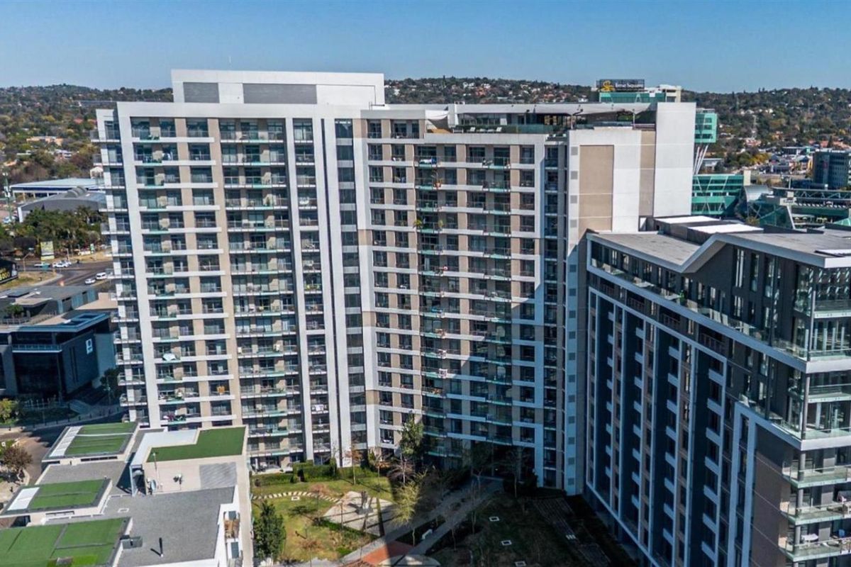 Aerial view of a modern high-rise apartment complex featuring multiple balconies and landscaped ground-level garden areas.
