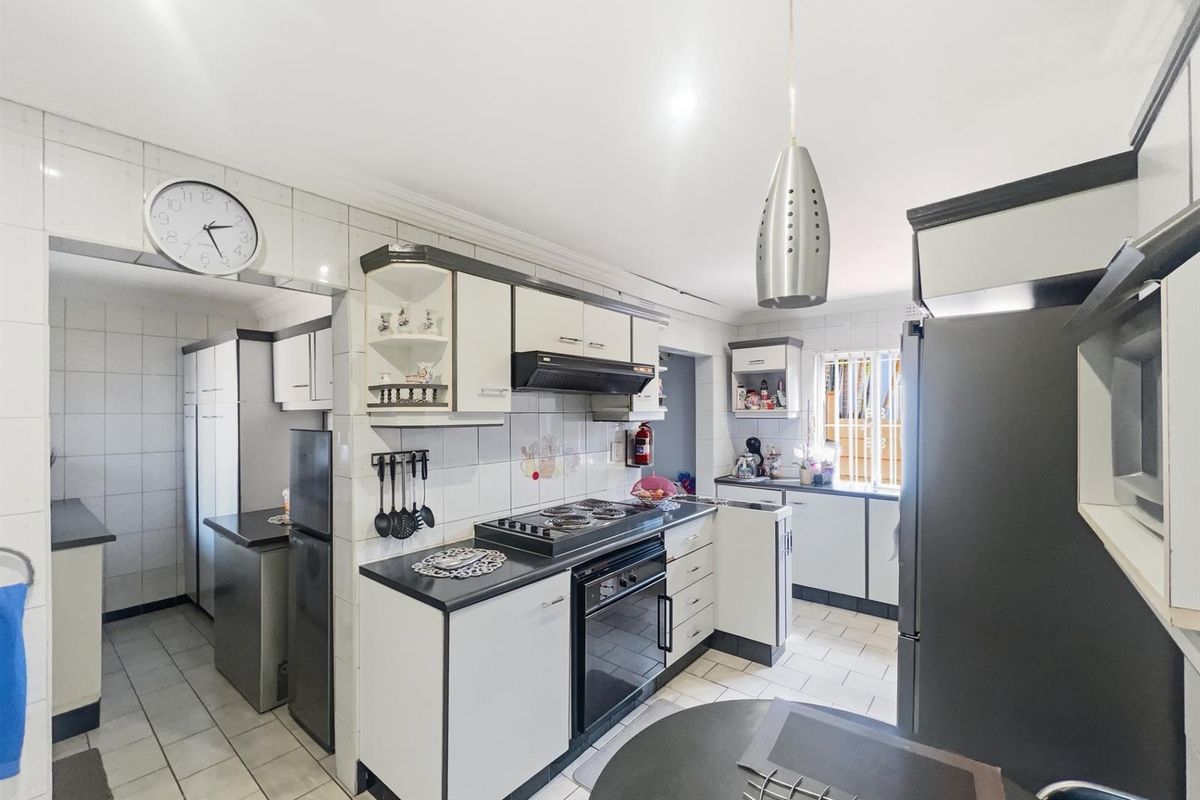 Functional kitchen featuring built-in cabinetry, integrated oven and hob, extractor fan, and tiled flooring with an adjacent scullery area.
