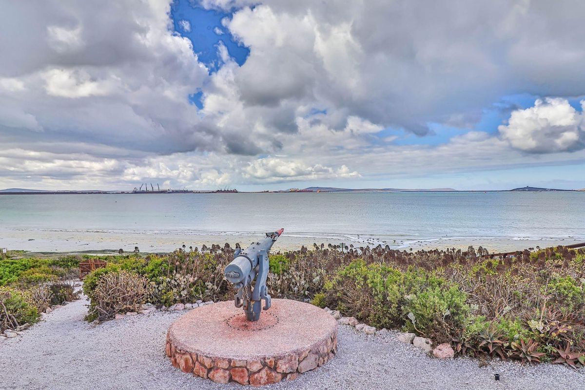 A scenic coastal view overlooking the bay, featuring a decorative historical cannon mounted on a stone plinth within a landscaped garden setting.