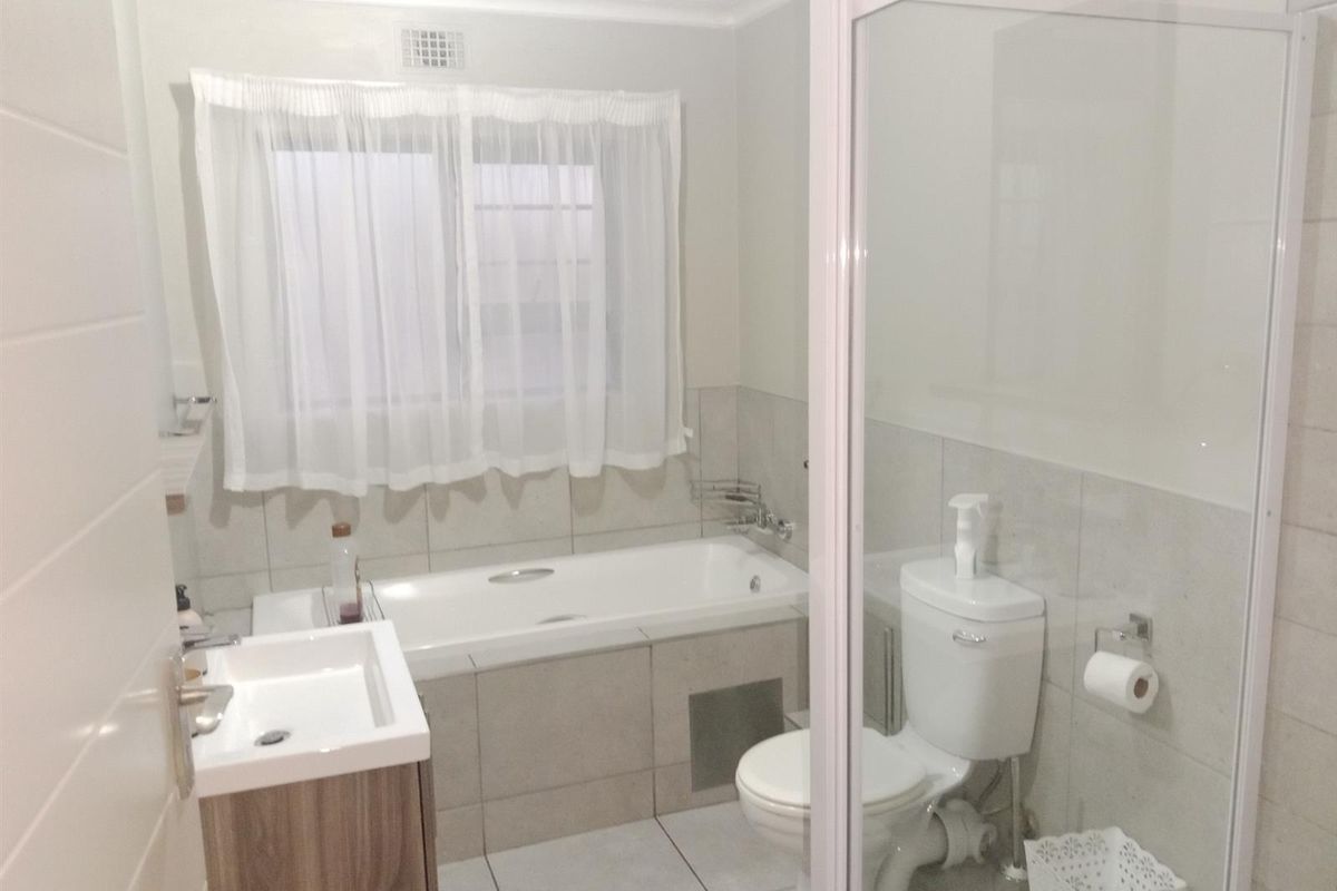 A functional bathroom featuring a built-in bathtub, separate shower enclosure, vanity basin, and toilet with neutral tiled finishes.