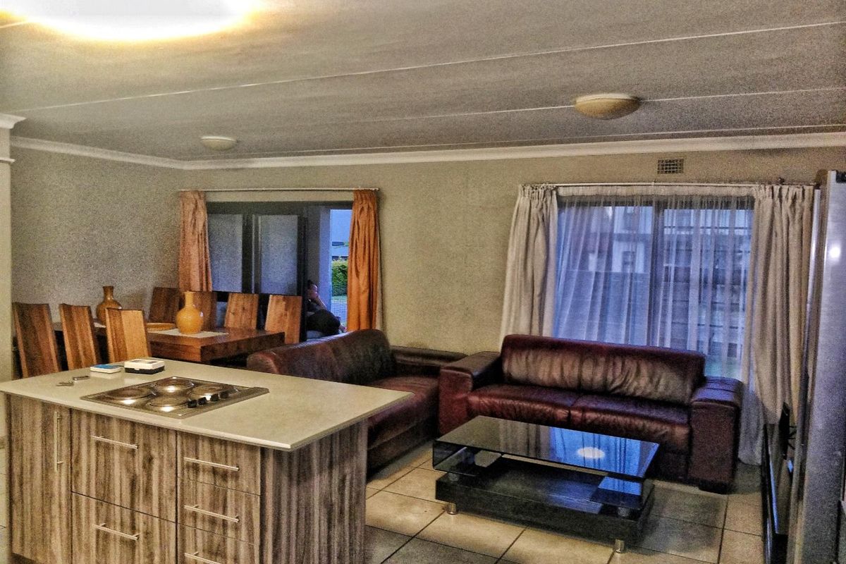 Open-plan living and dining area featuring a central kitchen island with a built-in hob, tiled flooring, and direct access to the exterior via sliding doors.