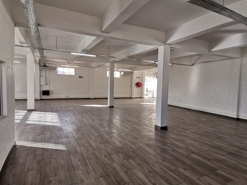 Spacious open-plan office area featuring wood-look tiled flooring, exposed structural beams, and integrated air conditioning units.