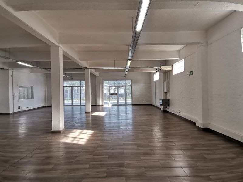 Spacious open-plan office area featuring wood-look tile flooring, exposed beam ceilings, and ample natural light through glass panel doors.