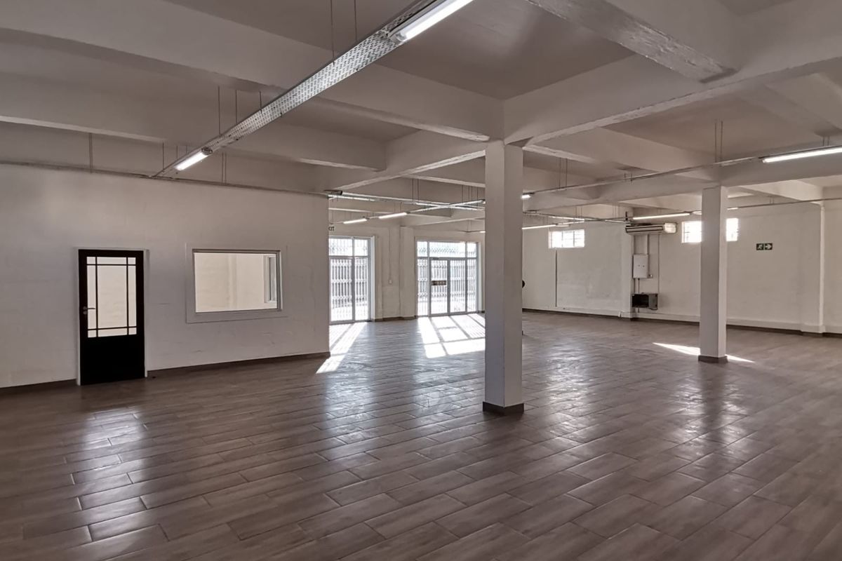 Spacious open-plan office area featuring tiled flooring, exposed structural beams, and ample natural light through multiple glass doors and windows.