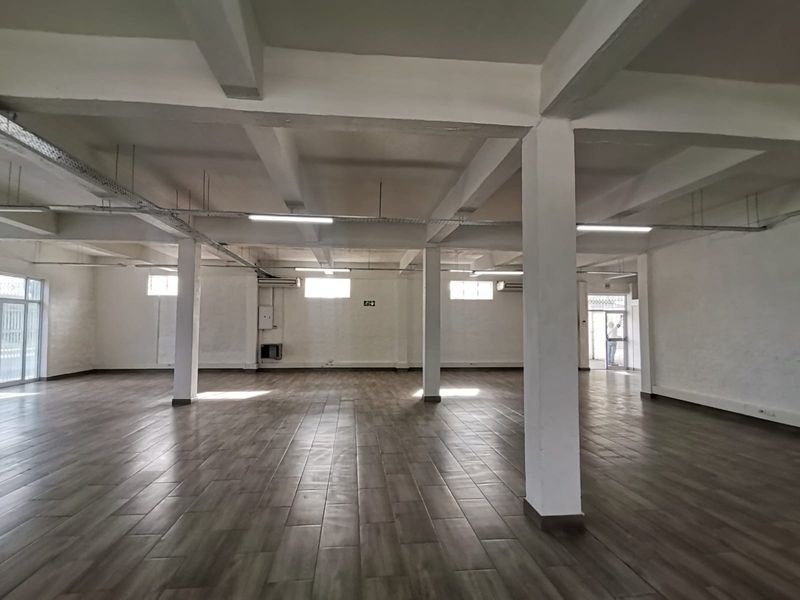 A spacious, open-plan office area featuring exposed concrete beams, tiled flooring, and integrated lighting, offering a versatile workspace ready for custom configuration.