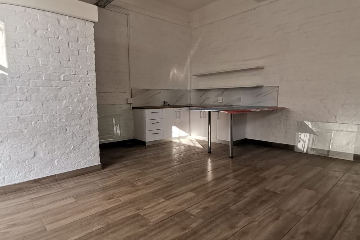 A compact office kitchenette featuring white cabinetry, marble-effect splashbacks, floating shelves, and wood-look tiled flooring within an industrial-style space.