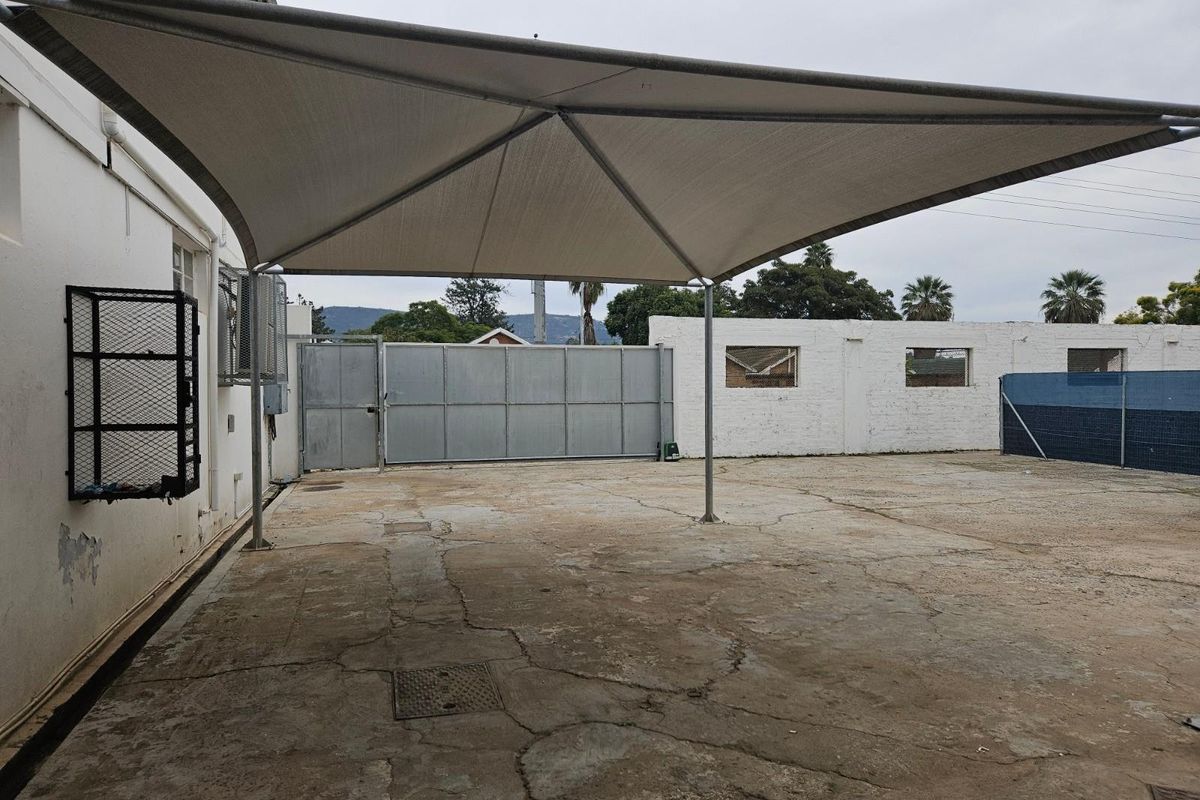 Exterior paved parking area featuring a large shade sail structure, perimeter boundary walls, and a metal access gate.