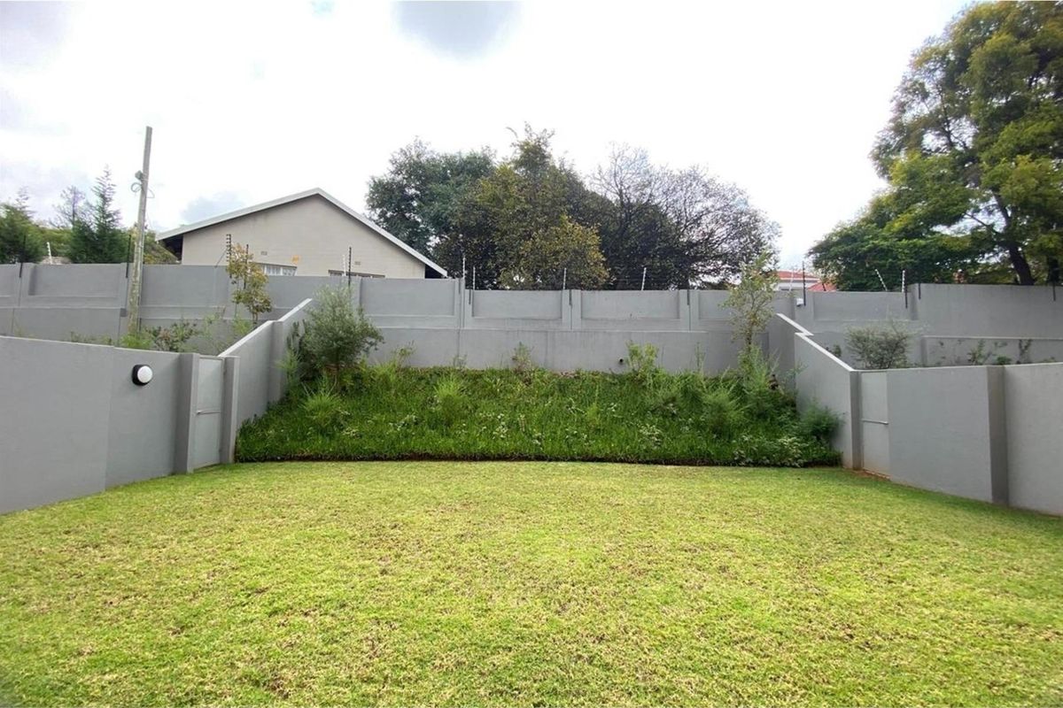 A private rear garden area featuring a well-maintained lawn, terraced landscaping, and high perimeter boundary walls with integrated electric fencing for added security.