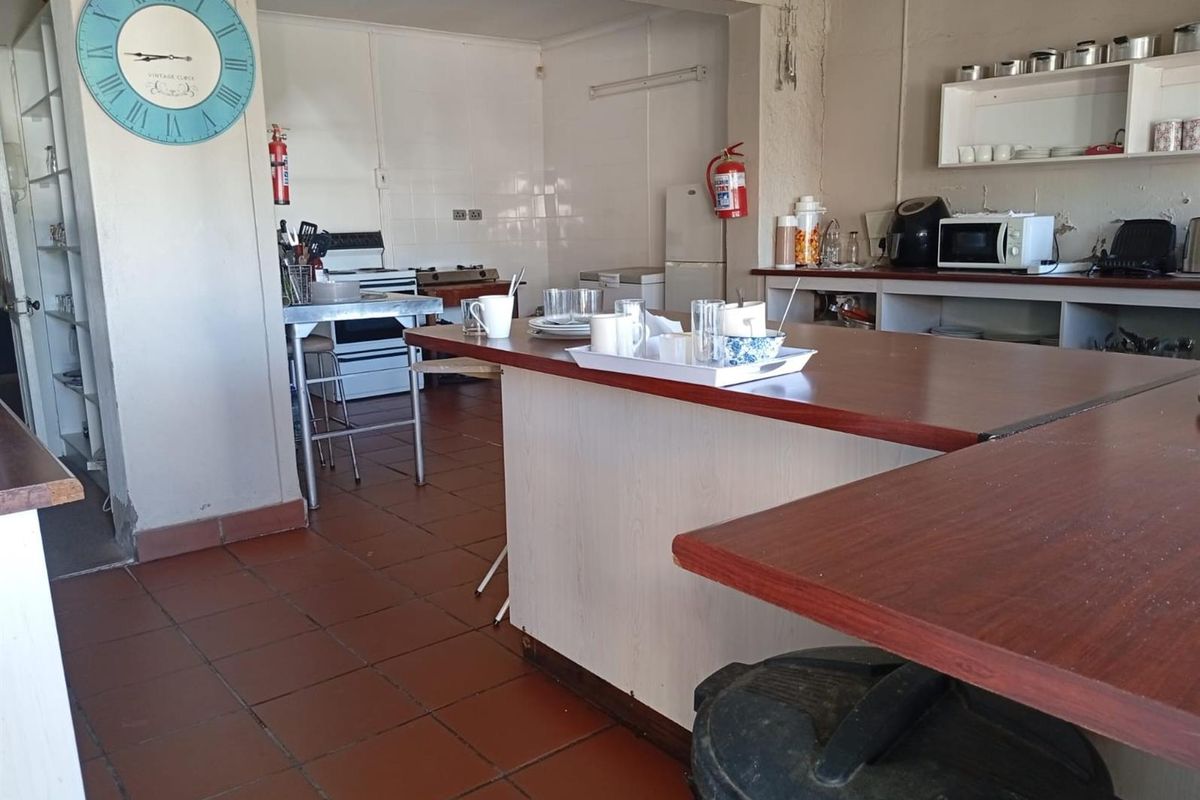 A functional kitchen area featuring a central breakfast counter, tiled flooring, and basic cabinetry, suitable for a guest house setting.