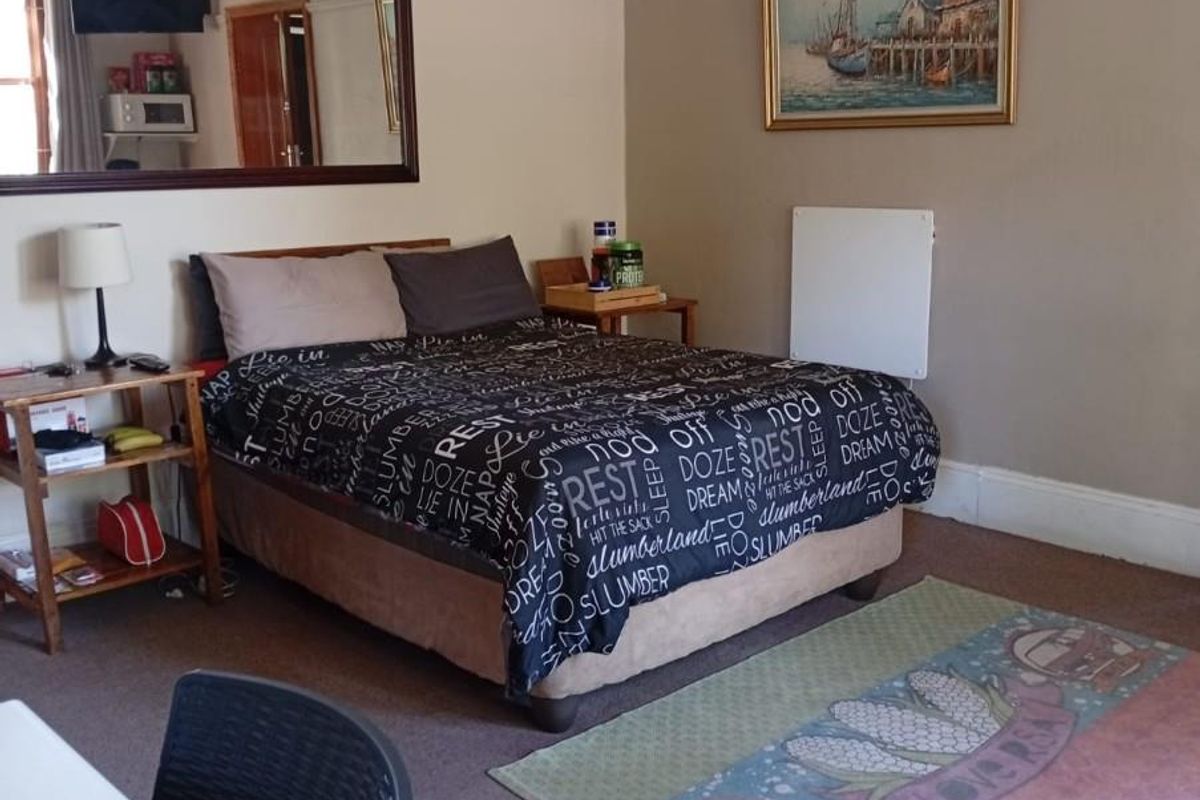 A bedroom featuring neutral wall tones, carpeted flooring, and a large wall-mounted mirror, providing a functional and comfortable sleeping space.