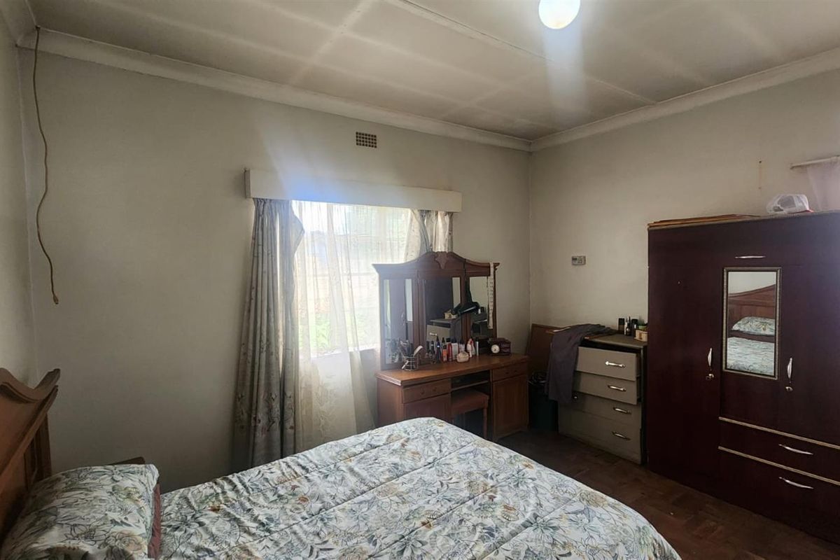A bedroom featuring a window with curtain pelmet, ceiling light fixture, and parquet flooring, requiring cosmetic updates to modernize the space.