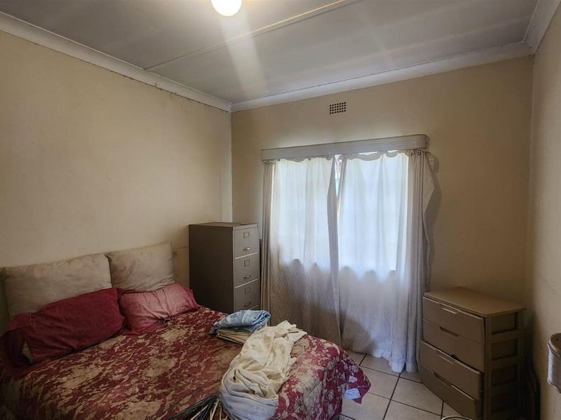 A standard bedroom featuring tiled flooring and a window with curtain fixtures, requiring cosmetic updates to improve its overall condition.