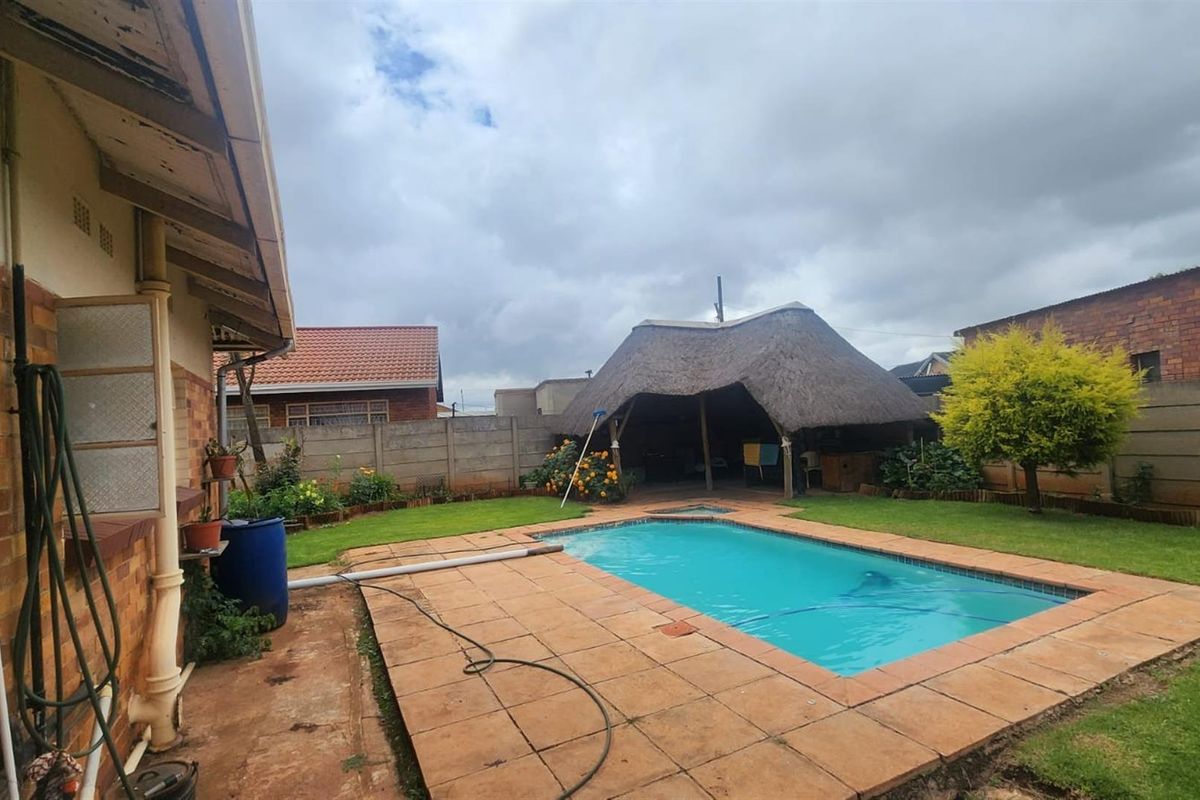Rear garden featuring a swimming pool, paved surround, and a thatched lapa entertainment area, enclosed by perimeter walling.