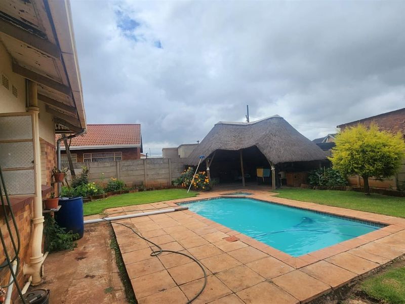 Rear garden featuring a swimming pool, paved surround, and a thatched lapa entertainment area, enclosed by perimeter walling.