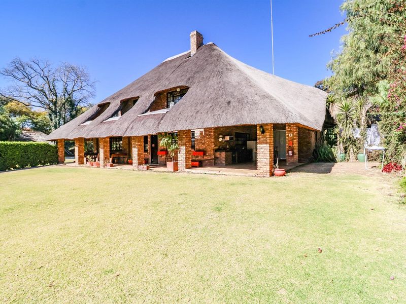 Rear view of a traditional thatched-roof house featuring a spacious covered brick patio overlooking a well-maintained garden.