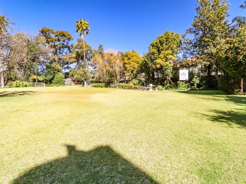 A spacious, well-maintained garden featuring a large manicured lawn surrounded by mature trees and established perimeter landscaping.