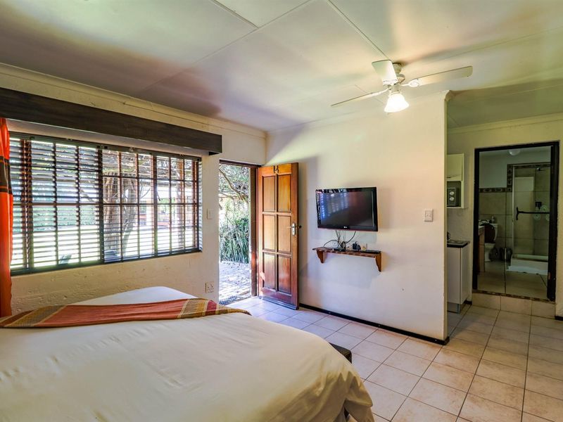 A bedroom featuring tiled flooring, a ceiling fan, and direct access to an en-suite bathroom, with natural light entering through a window and door.
