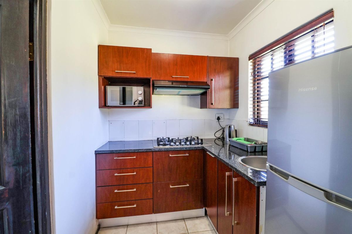 Compact kitchen featuring dark wood cabinetry, granite countertops, a gas hob with extractor fan, and built-in microwave, finished with tiled flooring.