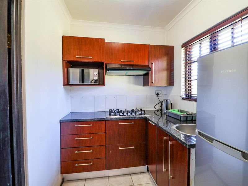Compact kitchen featuring dark wood cabinetry, granite countertops, a gas hob with extractor fan, and built-in microwave, finished with tiled flooring.
