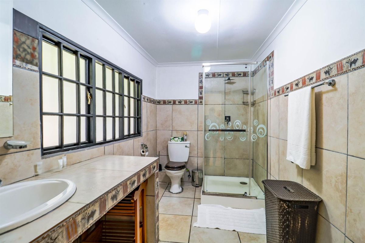 A functional bathroom featuring a tiled vanity, a glass-enclosed shower, and a toilet, finished with neutral wall tiles and a decorative border.