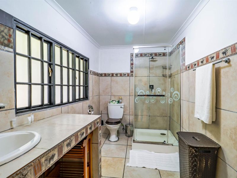 A functional bathroom featuring a tiled vanity, a glass-enclosed shower, and a toilet, finished with neutral wall tiles and a decorative border.