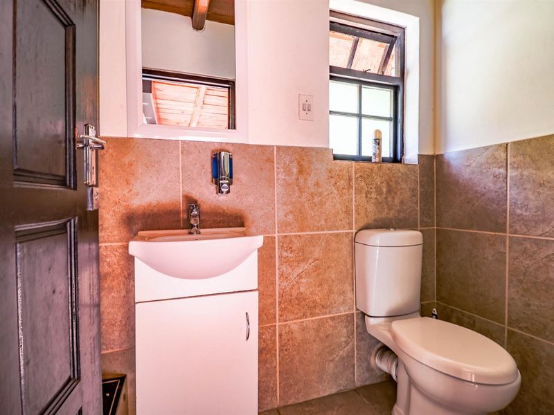 Compact bathroom featuring a vanity basin, toilet, and tiled walls with a small casement window for natural light.