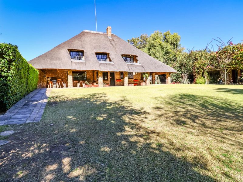A charming thatched-roof cottage featuring a brick facade, dormer windows, and a spacious covered patio overlooking a well-maintained garden.