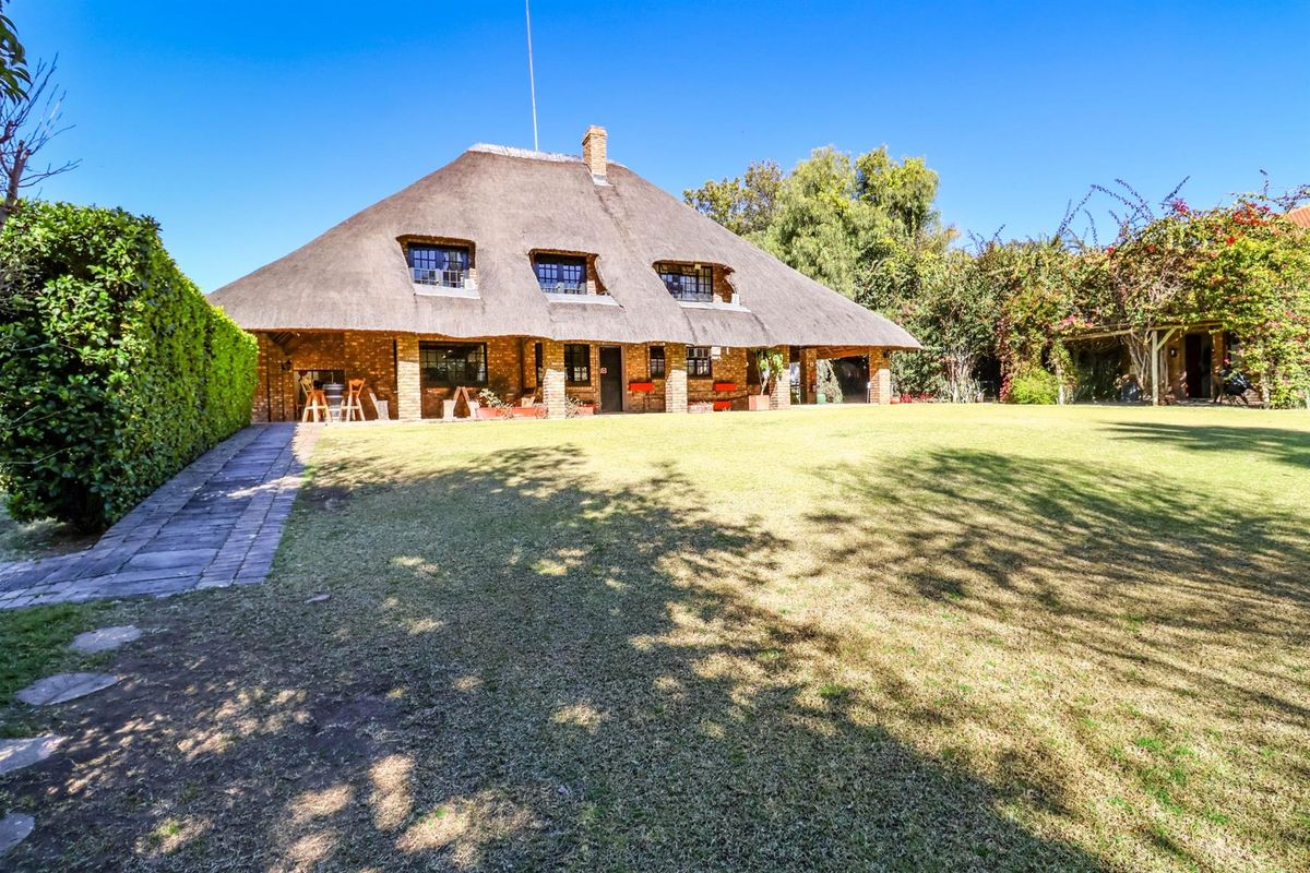 A charming thatched-roof cottage featuring a brick facade, dormer windows, and a spacious covered patio overlooking a well-maintained garden.