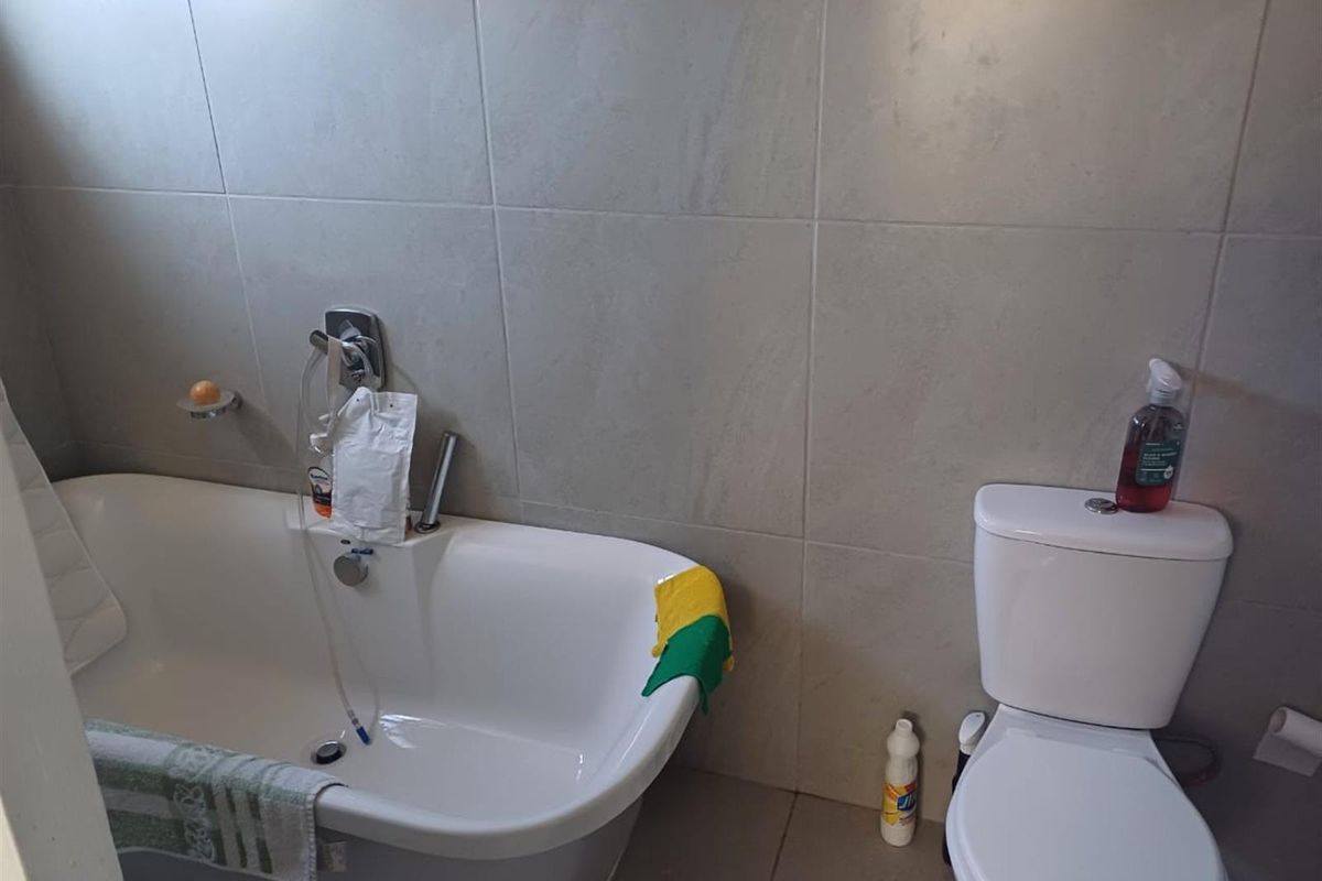 A functional bathroom featuring a white bathtub with chrome fixtures and a standard white toilet against neutral wall tiling.