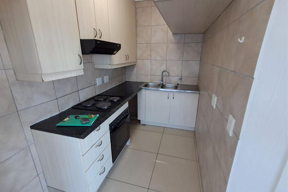 A compact kitchen featuring light-toned cabinetry, dark granite countertops, a built-in electric hob and oven, and tiled flooring and splashbacks.