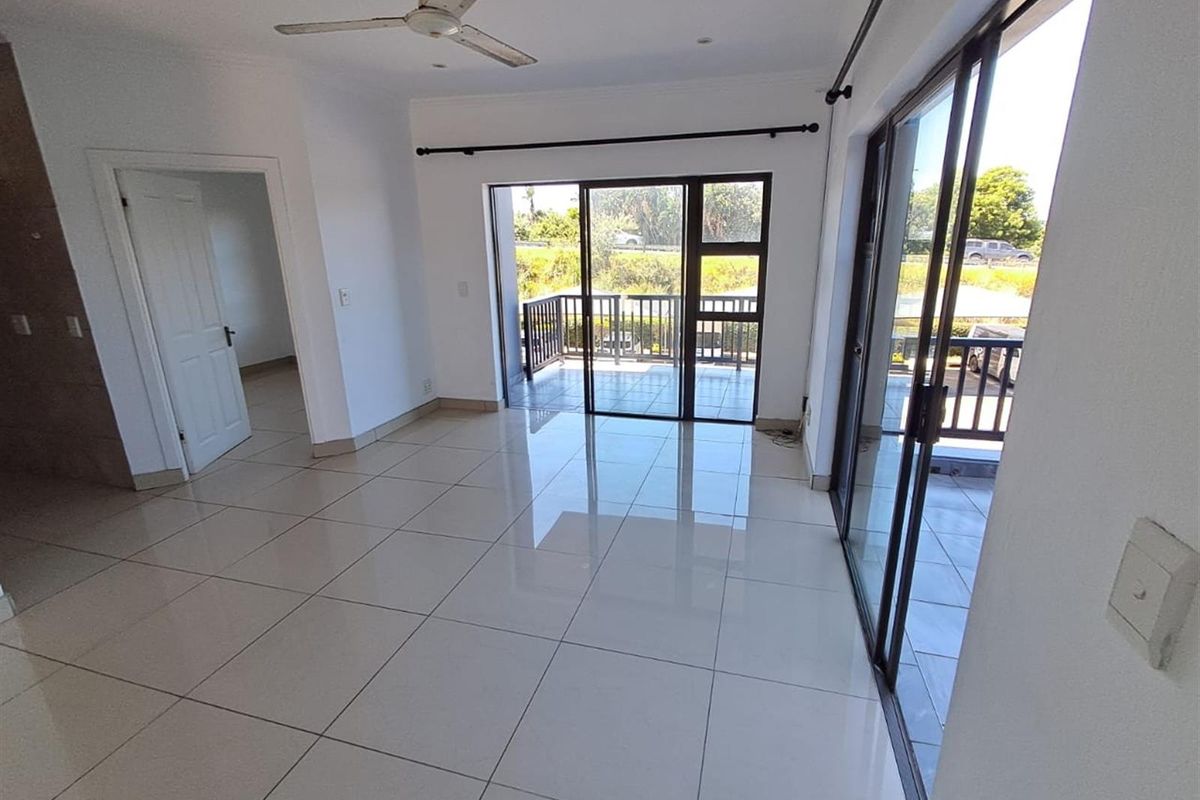 Bright and spacious living area featuring large sliding glass doors that open onto a private balcony, complemented by polished floor tiles and ceiling fan.