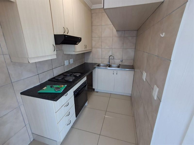 A compact kitchen featuring light-toned cabinetry, dark granite countertops, a built-in electric hob and oven, and tiled flooring and splashbacks.