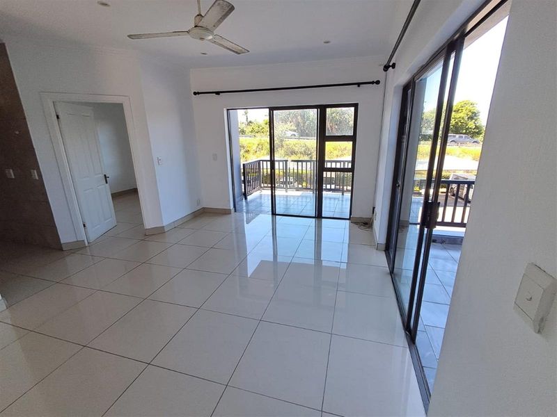Bright and spacious living area featuring large sliding glass doors that open onto a private balcony, complemented by polished floor tiles and ceiling fan.