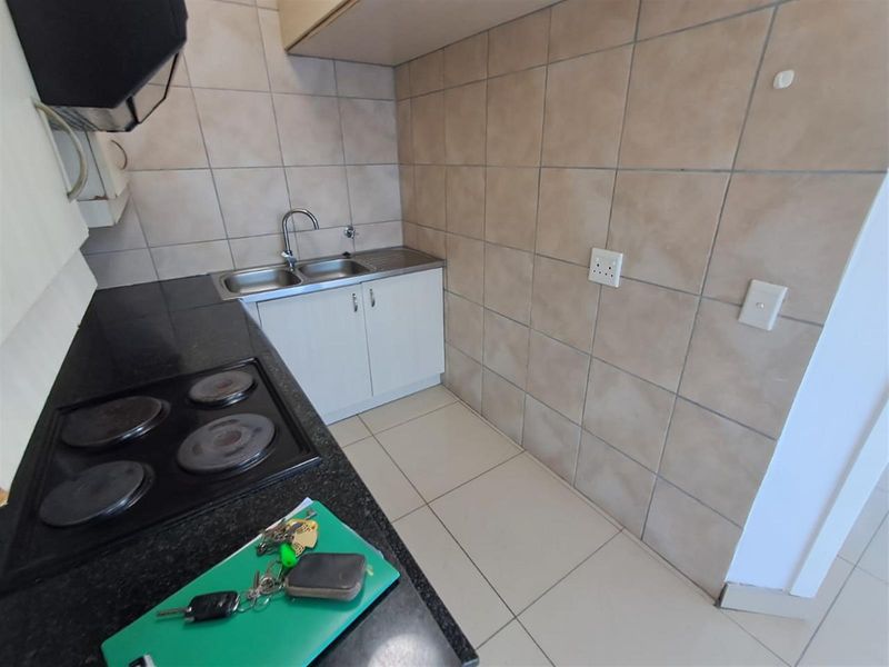 A compact kitchen featuring dark granite countertops, a built-in electric hob, stainless steel double sink, and tiled splashbacks.