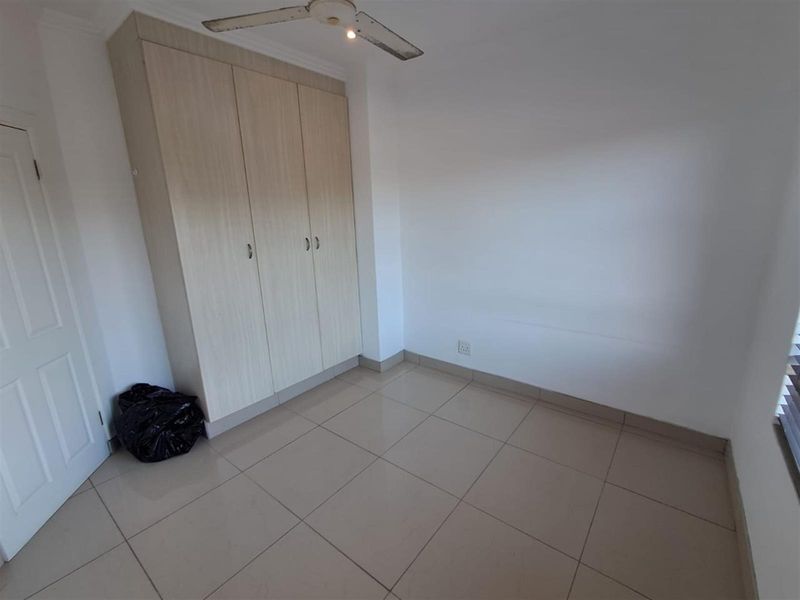 A bright, empty bedroom featuring neutral floor tiles, built-in wooden cabinetry, and a ceiling fan.