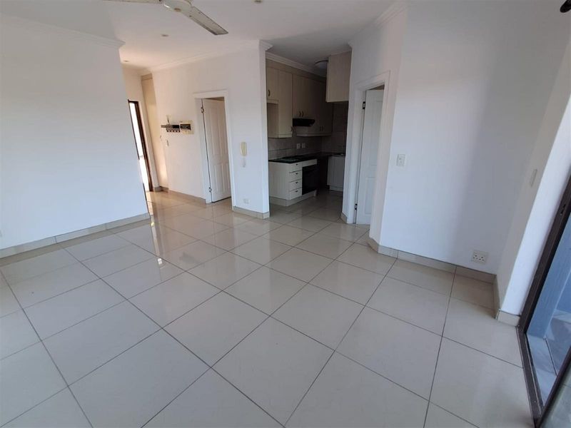 An open-plan living area featuring tiled flooring, leading into a compact kitchen equipped with built-in cabinetry and a stove.