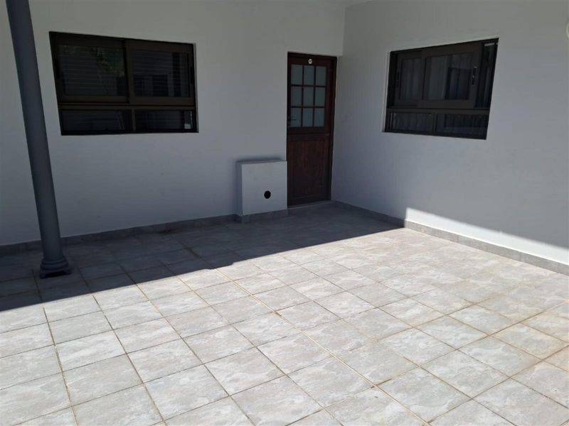 A covered patio area featuring tiled flooring, dark-framed windows, and a wooden entrance door, providing a functional outdoor space.