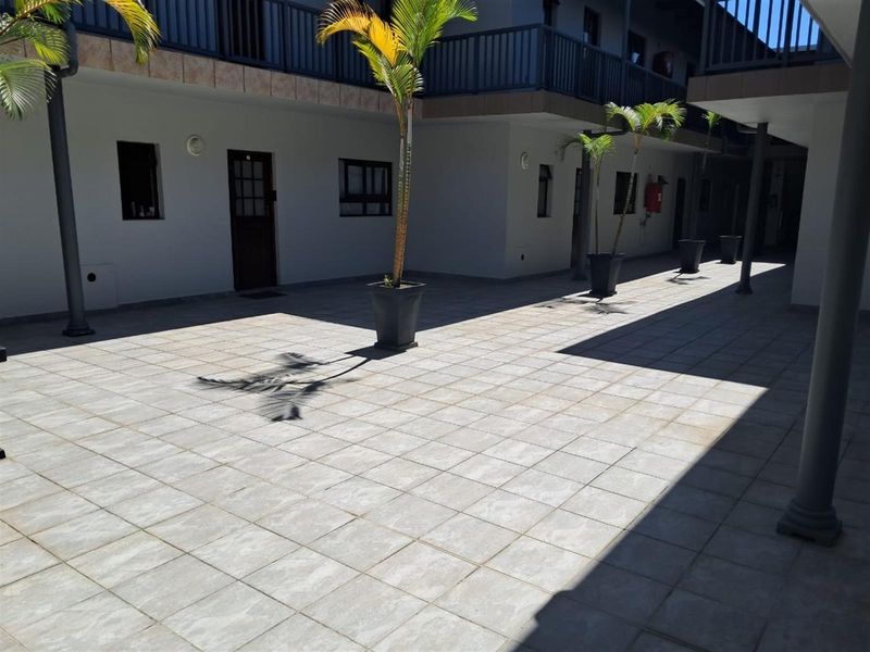 A paved outdoor courtyard area within an apartment complex, featuring tiled flooring, structural pillars, and access to multiple unit entrances.