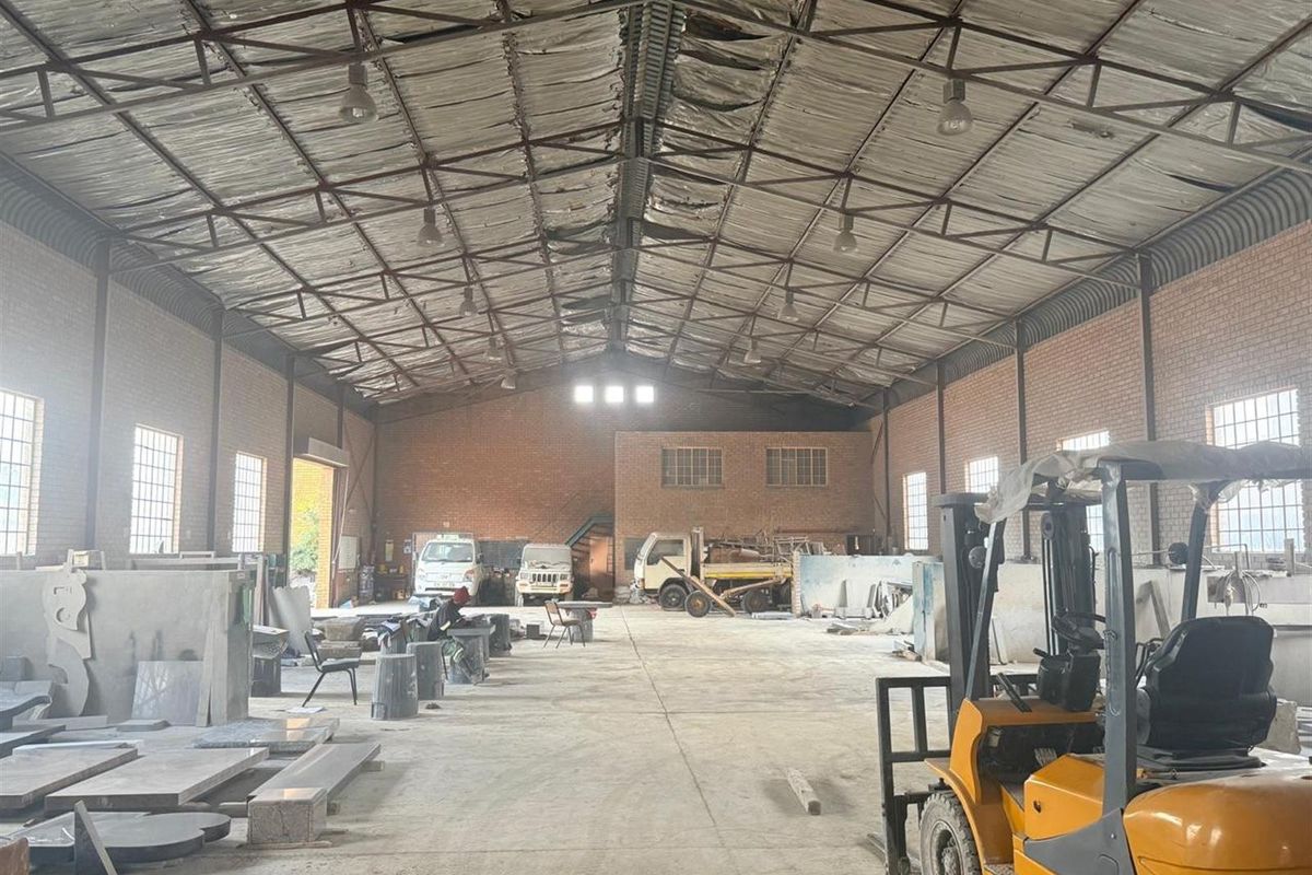 Spacious industrial warehouse featuring high ceilings with exposed steel trusses, brick walls, and concrete flooring, suitable for manufacturing or storage operations.