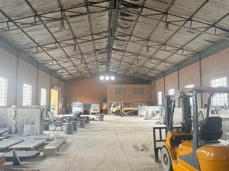 Spacious industrial warehouse featuring high ceilings with exposed steel trusses, brick walls, and concrete flooring, suitable for manufacturing or storage operations.