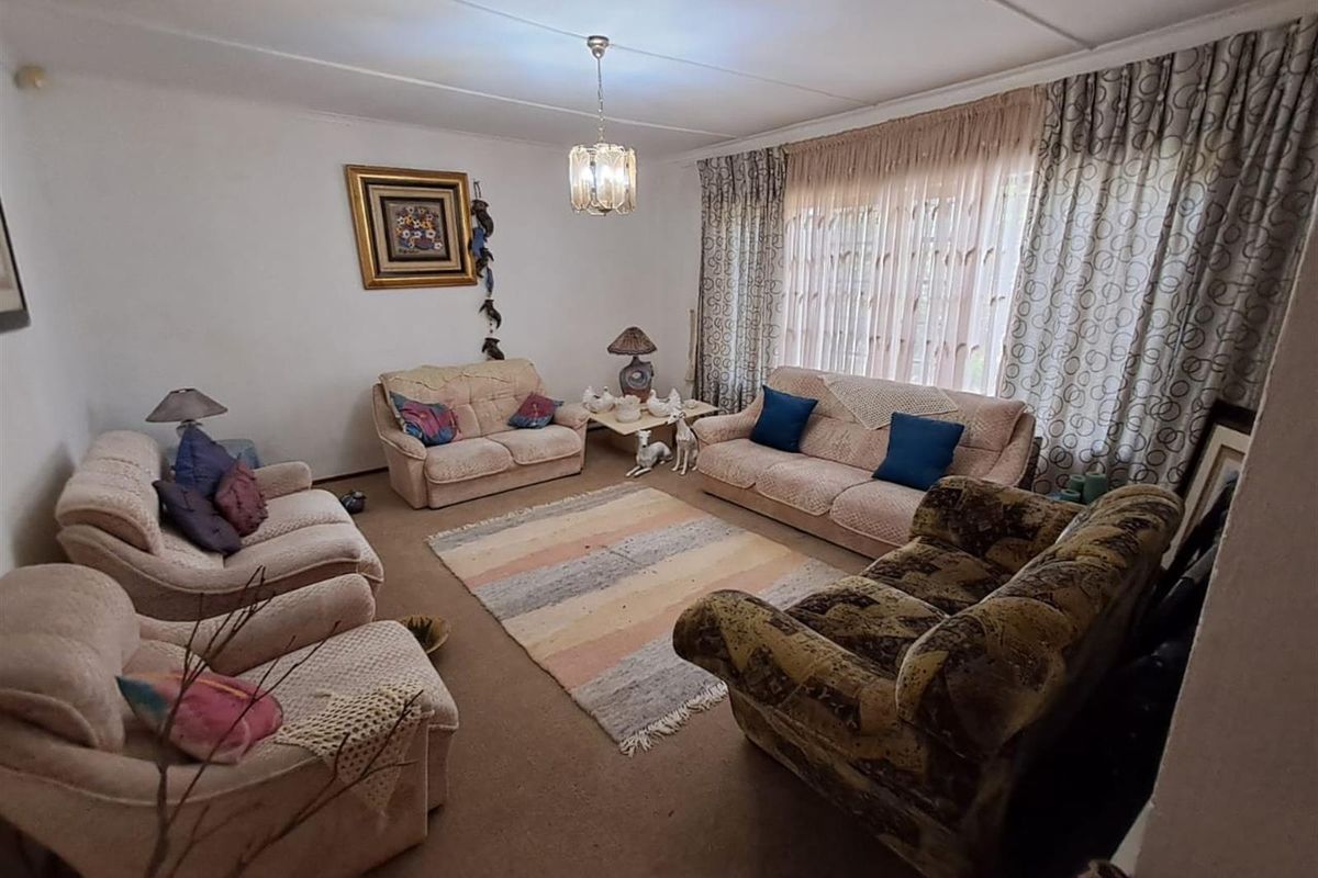 A spacious living room featuring carpeted flooring, a central light fixture, and large windows with curtains, offering a comfortable and traditional living space.