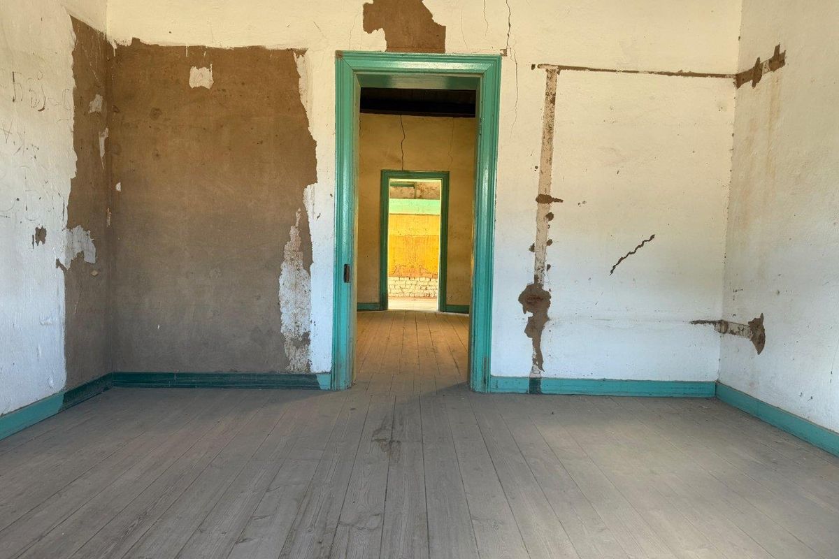 An empty, dilapidated interior room featuring original timber flooring and damaged wall plaster, showing significant signs of wear and requiring extensive renovation.