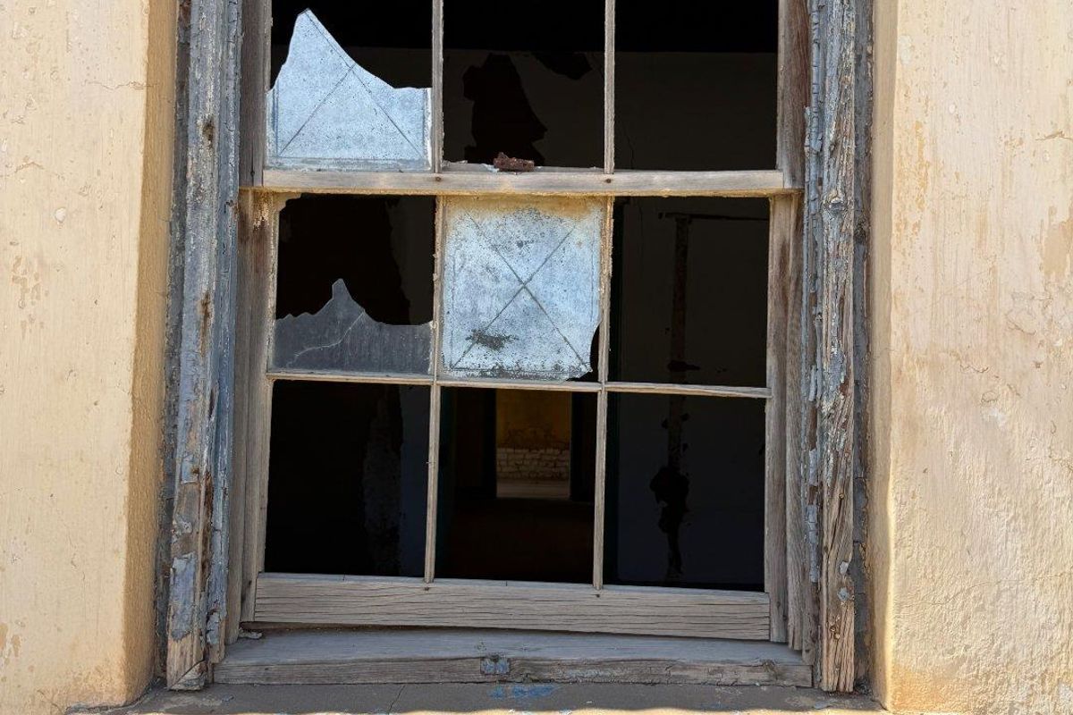A close-up view of a severely weathered, multi-pane wooden window with broken glass and peeling paint on the surrounding exterior wall.